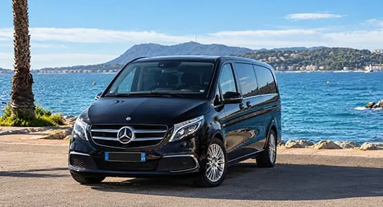 Van Mercedes noir stationné au bord de la mer, face aux collines.