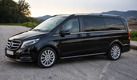 Van Mercedes noir stationné sur une route avec des collines en arrière-plan.